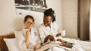 Two people in white robes sitting on a bed with a magazine, a pillow, and a cup. - Hotel McCoy Tucson - Art, Coffee, Beer, Wine (Tucson)