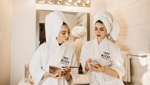 Two individuals in white robes with "Hotel McCoy" text, standing in a bathroom with a mirror, vanity, and toiletries. - Hotel McCoy Tucson - Art, Coffee, Beer, Wine (Tucson)