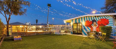 A well-lit outdoor area with string lights, a mural, and a seating area with chairs and tables.