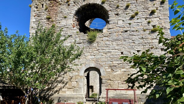 An outdoor seating area with tables and chairs in front of a stone building with a large arched window. - Hotell St Clemens (Visby)