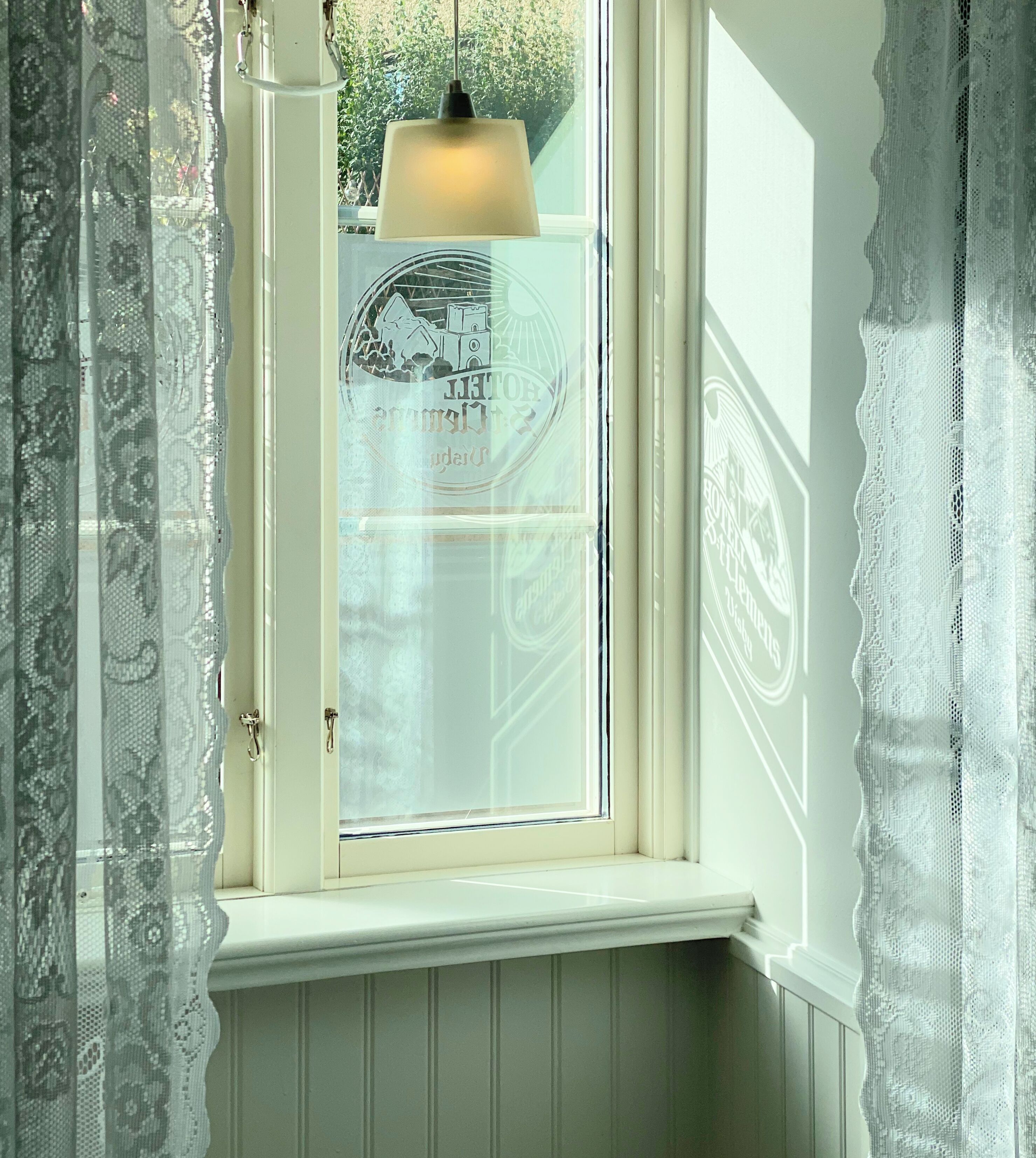 Ett fönster med en vit ram, en vit lampa inuti och utsikt över en byggnad med en solsymbol och text.