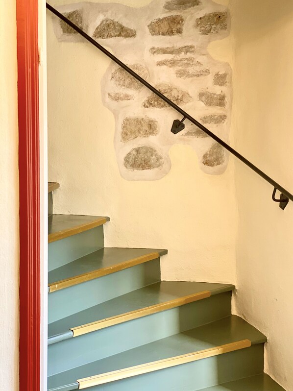 A staircase with blue steps and a handrail, leading to a wall with a stone-like texture.