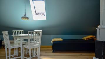 A room with a dining table and chairs, a dark sofa with cushions, and a window with a view.