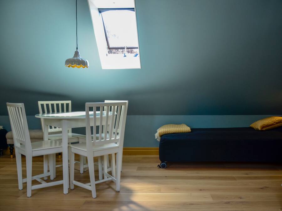 A room with a dining table and chairs, a dark sofa with cushions, and a window with a view.