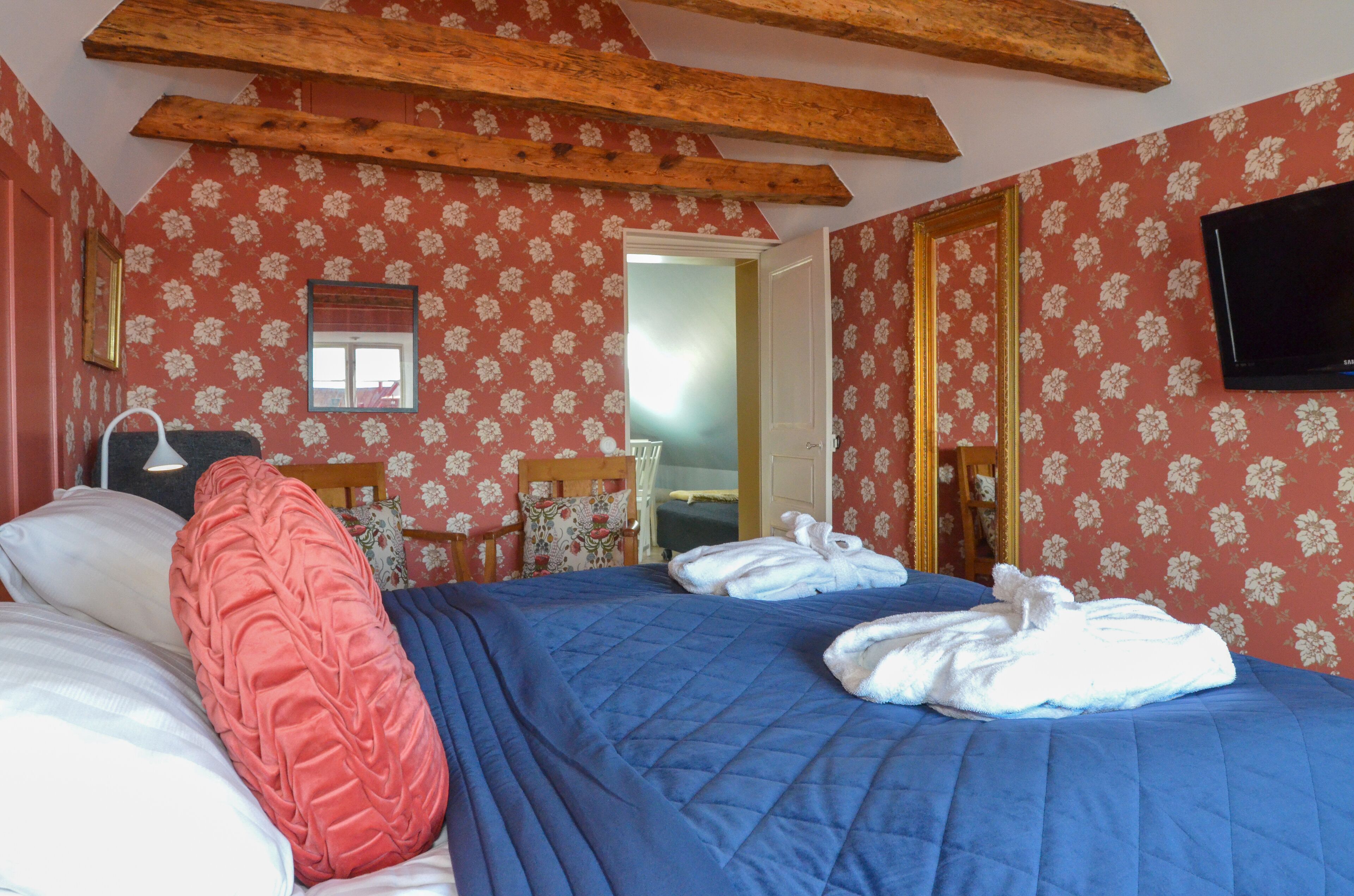 A bedroom with a bed, pillows, a wooden ceiling beam, a mirror, and a television.