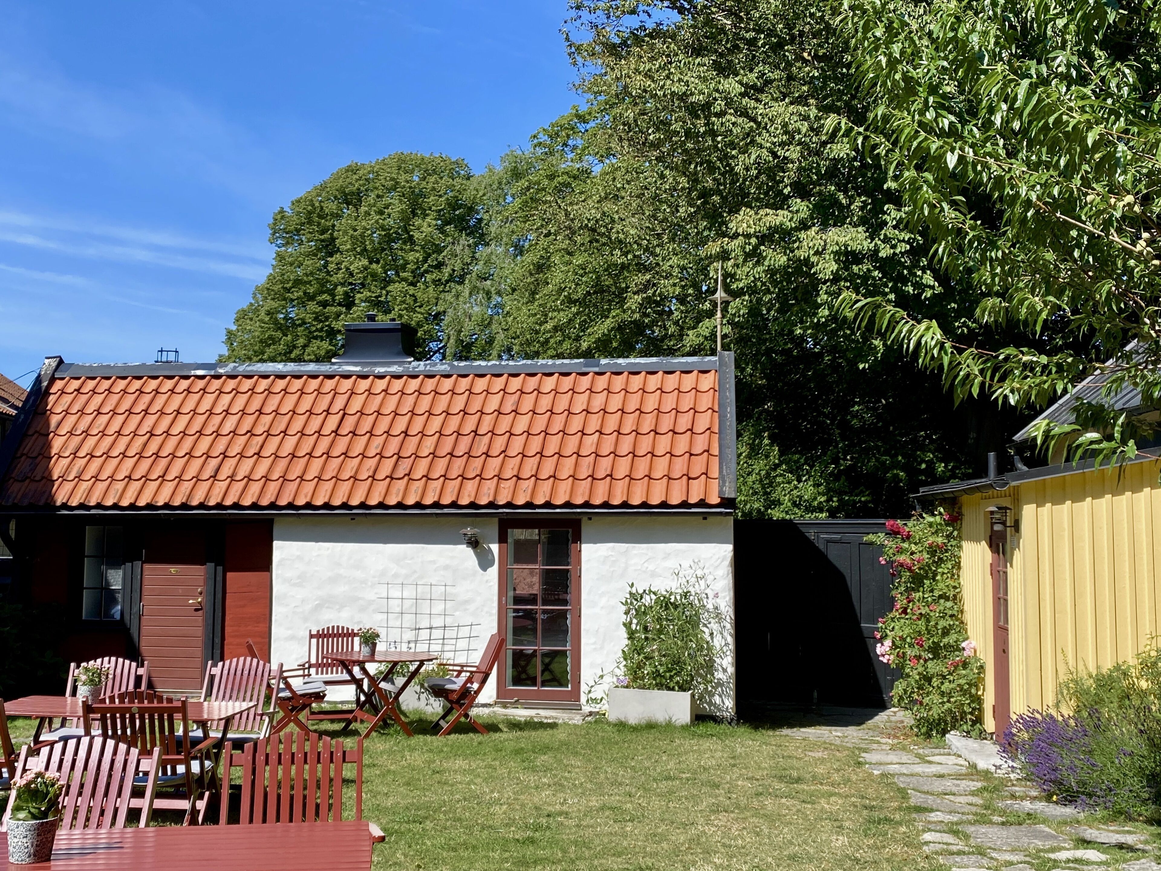 Een huis met een pannendak, een witte gevel en een kleine tuin met een tafel en stoelen.