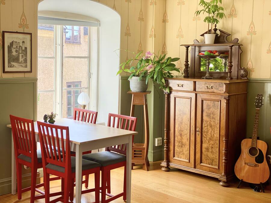 A dining area with a table and chairs, a cabinet with a guitar, and a window with a view of buildings.