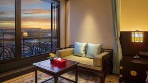 Habitación de hotel con un ventanal grande que ofrece vistas panorámicas, un sofá con cojines, una mesita con una caja de pañuelos y una lámpara.