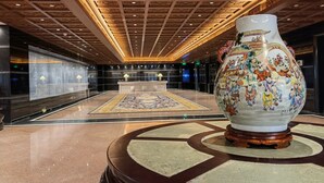 Un vestíbulo con un gran jarrón decorativo, una alfombra estampada y un techo con elaborados detalles de madera.