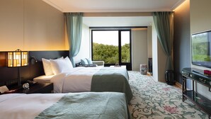 Habitación de hotel con dos camas, televisión, escritorio y un ventanal grande con cortinas.