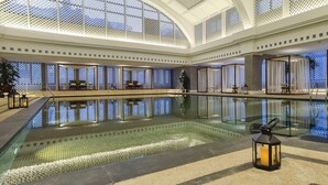 A large indoor pool with clear water, surrounded by seating areas and a high ceiling with decorative lattice. - Grand Hotel Beijing   (Beijing)