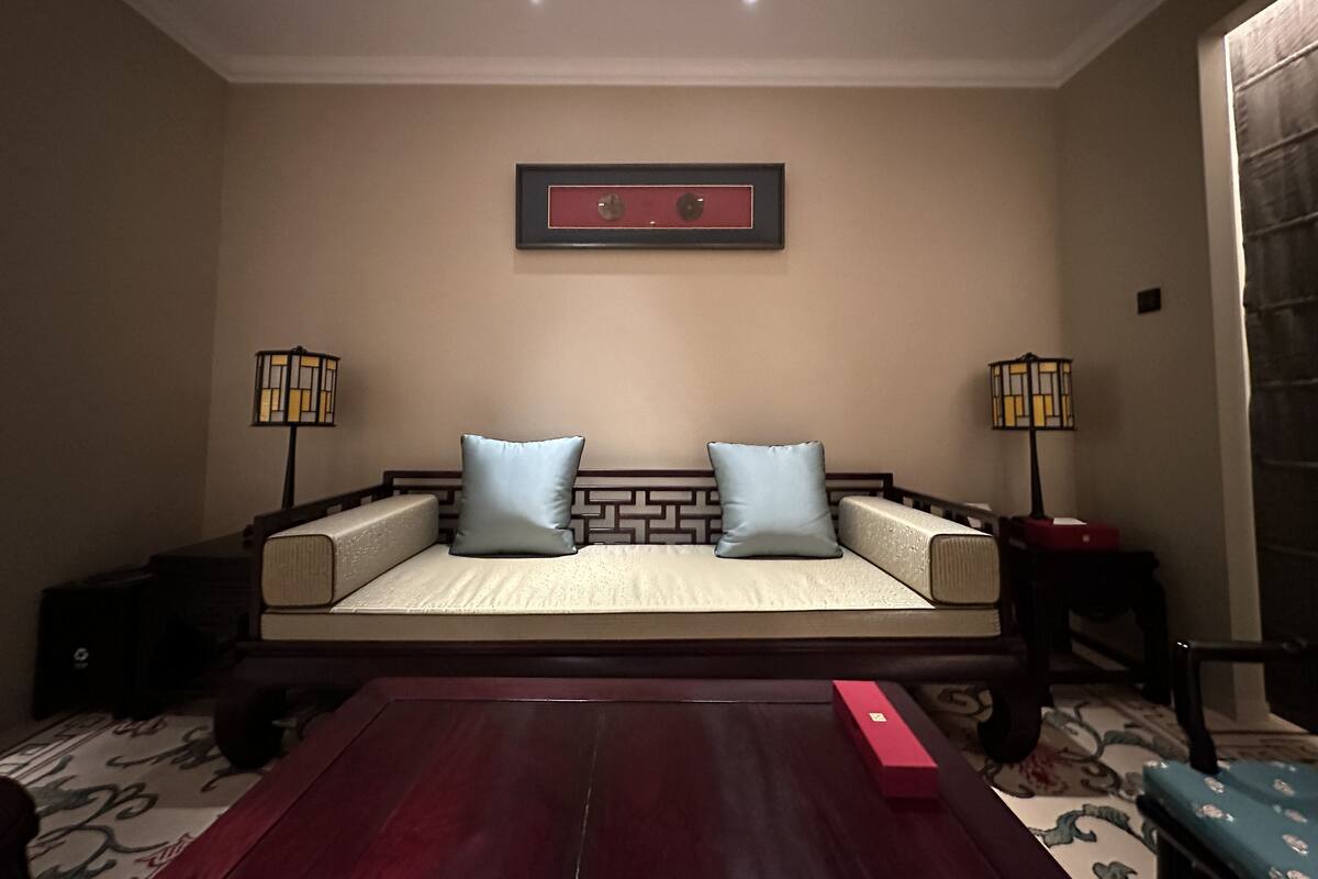 A room with a sofa bed, two floor lamps, a framed picture on the wall, and a patterned carpet.