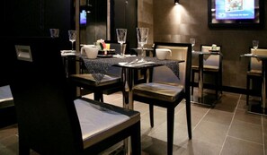 A restaurant with tables set for dining, chairs, and a television screen in the background. - L'adresse (Paris)