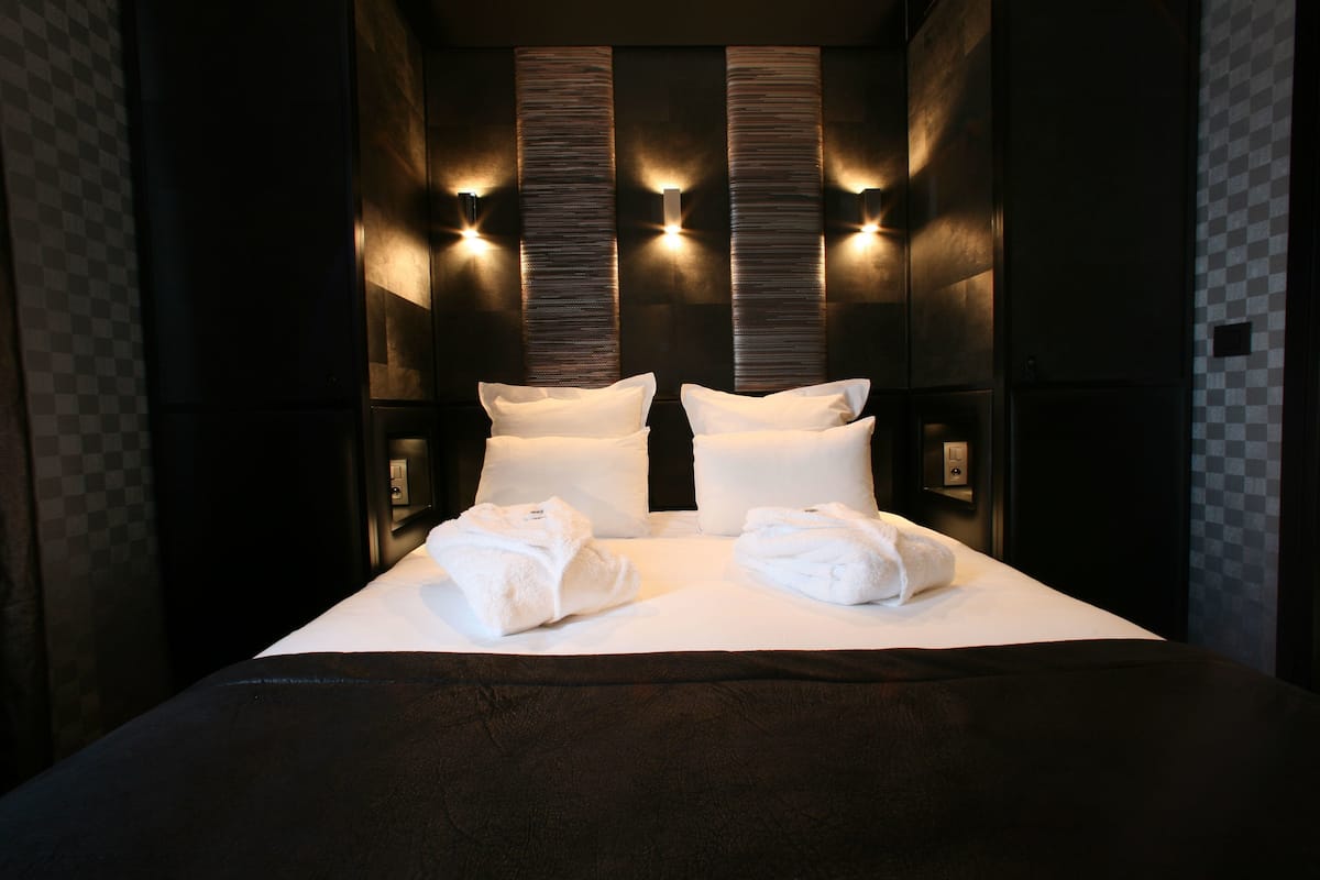 Une chambre d’hôtel avec un grand lit, deux lampes fixées au mur et un motif à carreaux sur le mur.