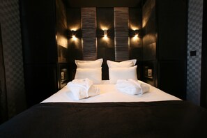 Una habitación de hotel con una cama grande, dos lámparas de pared y un estampado de cuadros en la pared.