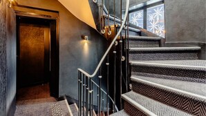 A modern staircase with a black railing and patterned steps, leading to an elevator. - L'adresse (Paris)