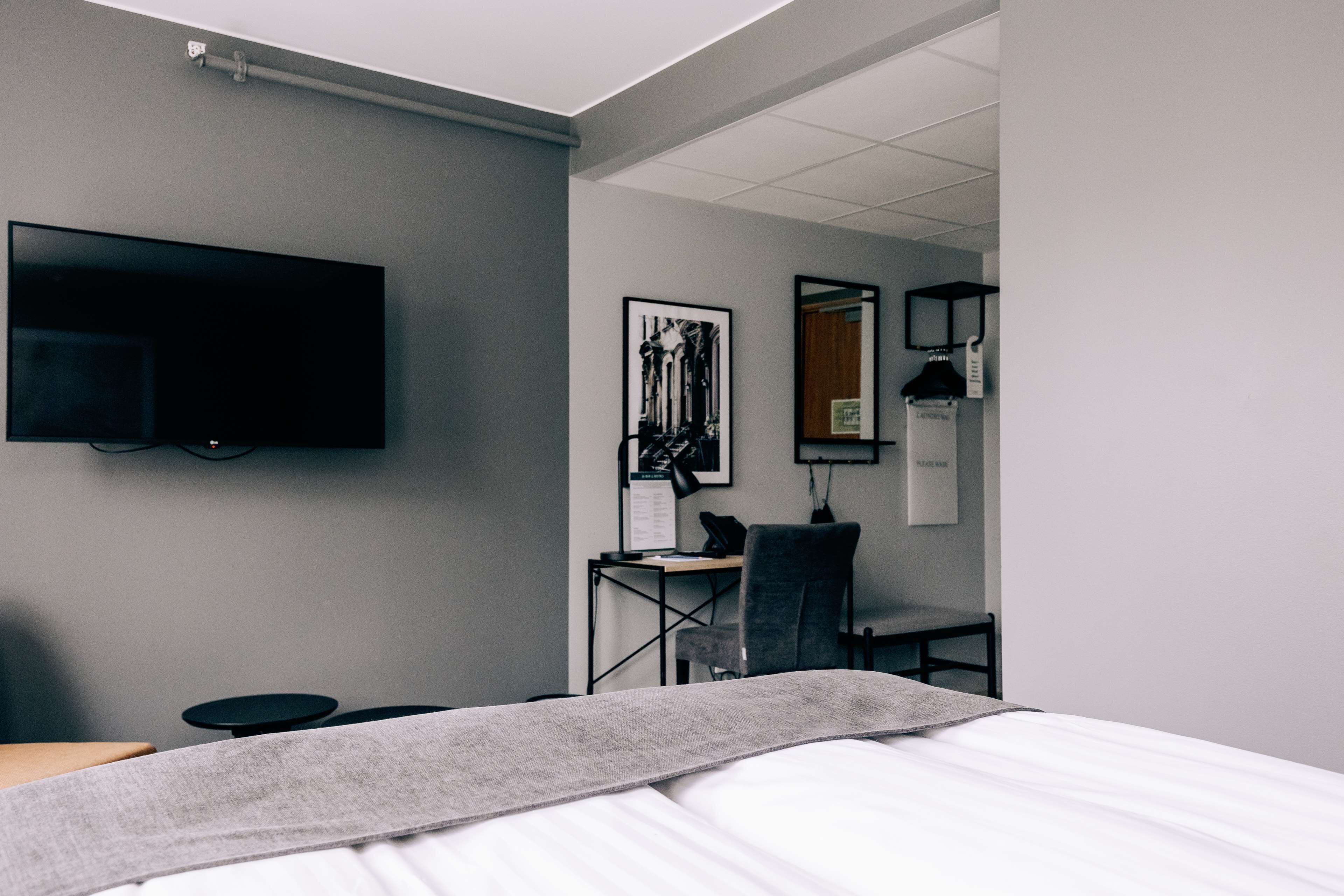A hotel room with a bed, a desk with a chair, a flat-screen TV mounted on the wall, and a framed picture on the wall.