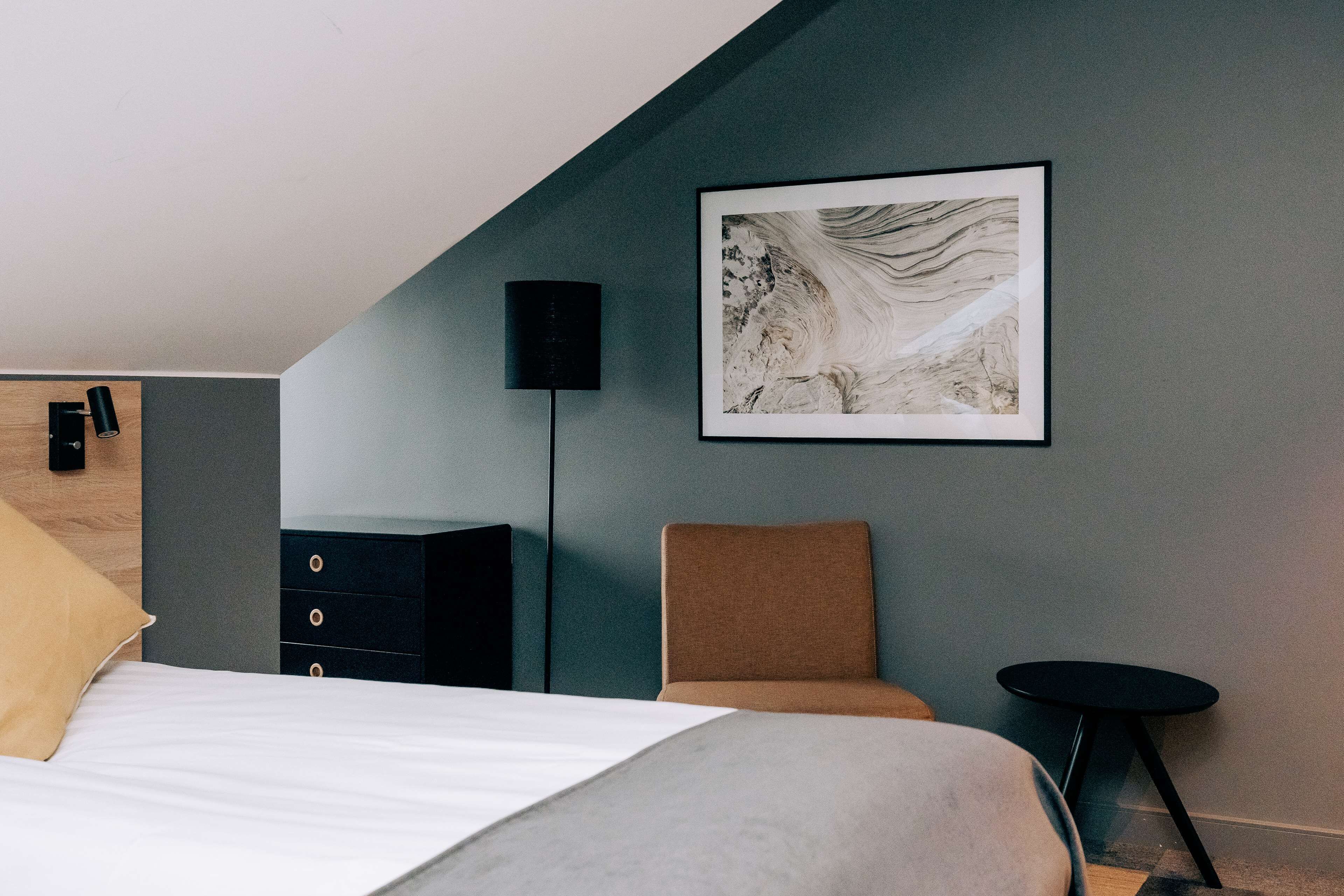 Une chambre à coucher moderne comprenant un lit, une commode, une chaise, une petite table et un haut-parleur fixé au mur.