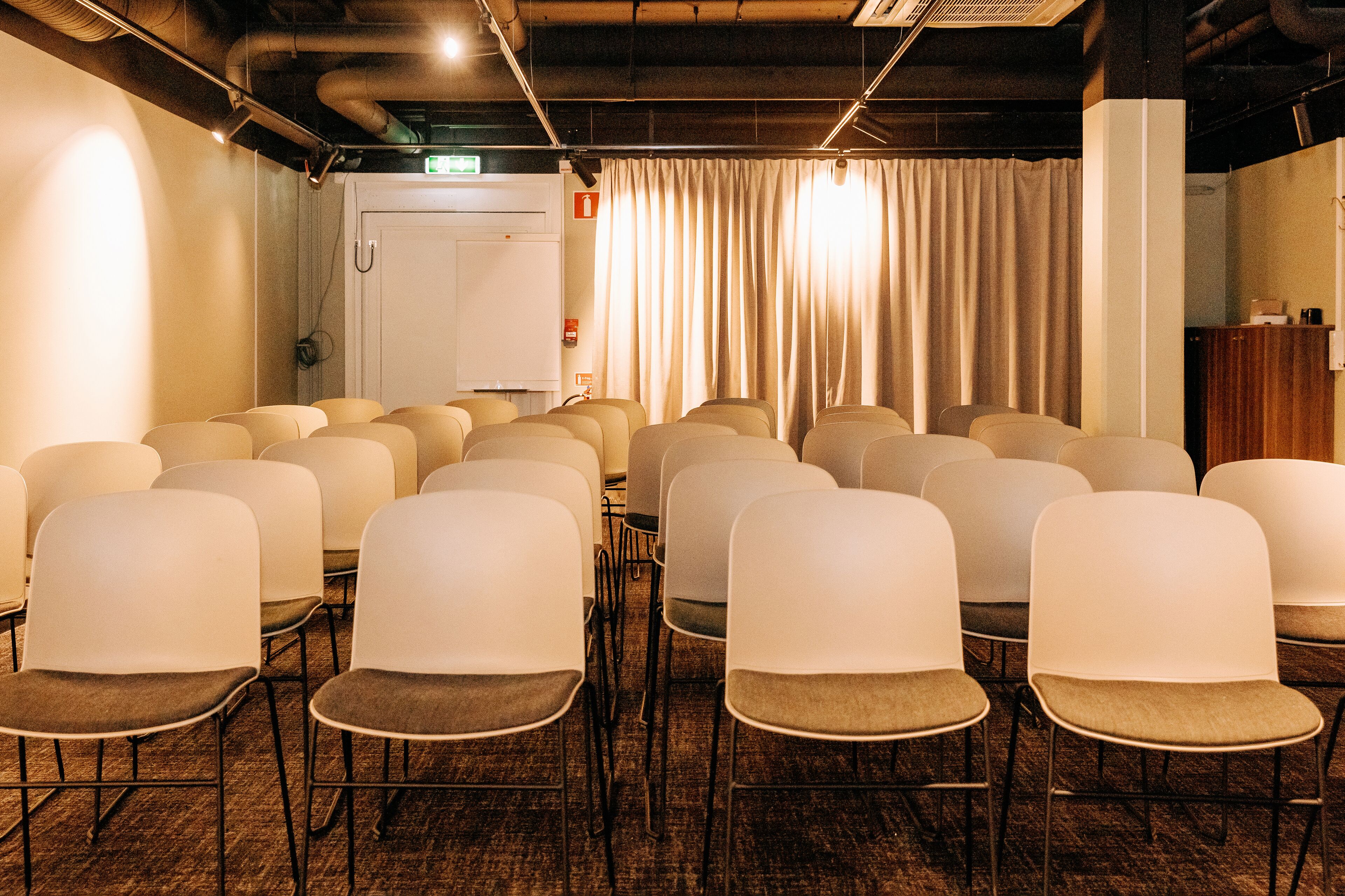A conference room with rows of chairs, a whiteboard, and a curtain.