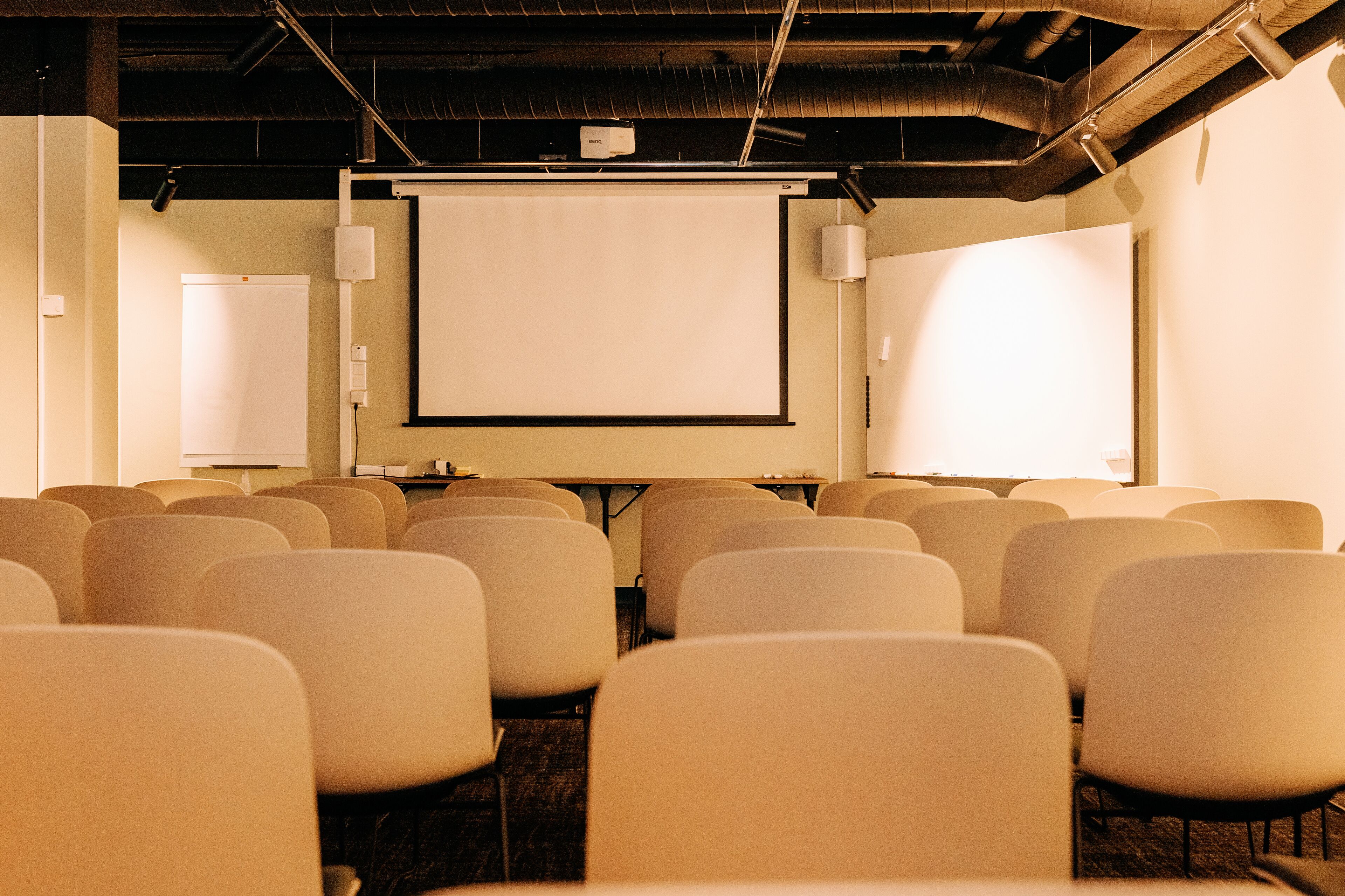 A conference room with rows of chairs facing a projection screen, equipped with a projector and a screen.