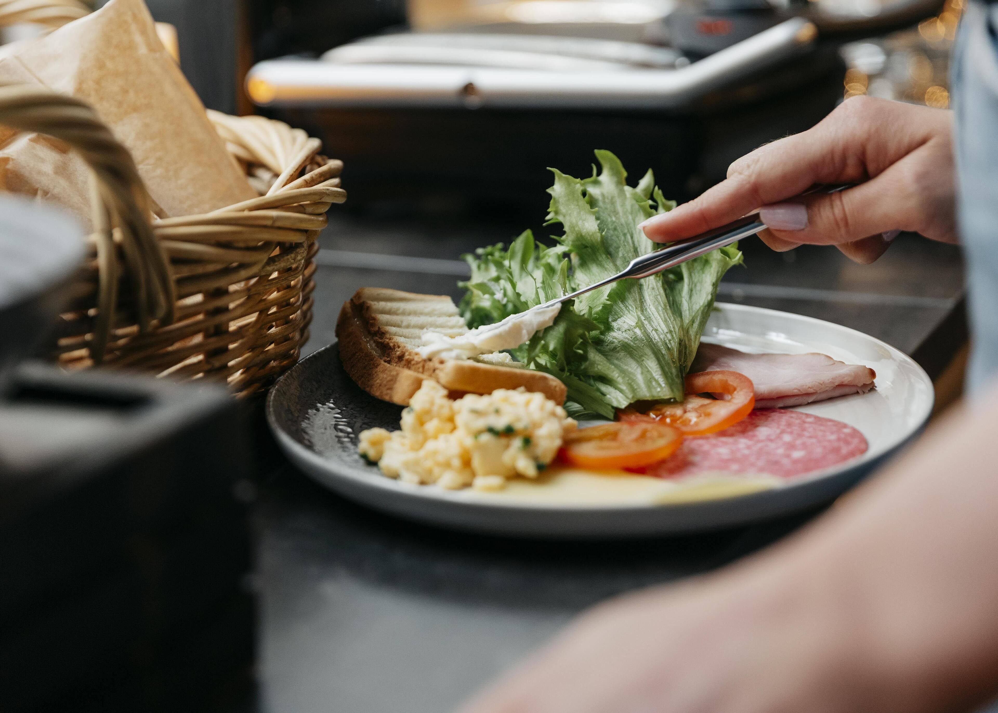 Une assiette contenant des œufs brouillés, des tomates en tranches, de la laitue et une tranche de jambon.
