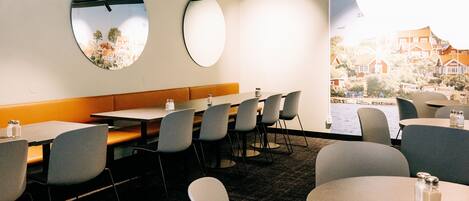 A modern dining area with round tables, comfortable seating, and a view of a town through large windows.
