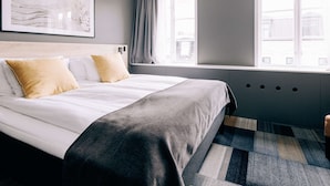 Et moderne hotelværelse med en stor seng, et vindue med gardiner, en sengegavl og et billede på væggen.