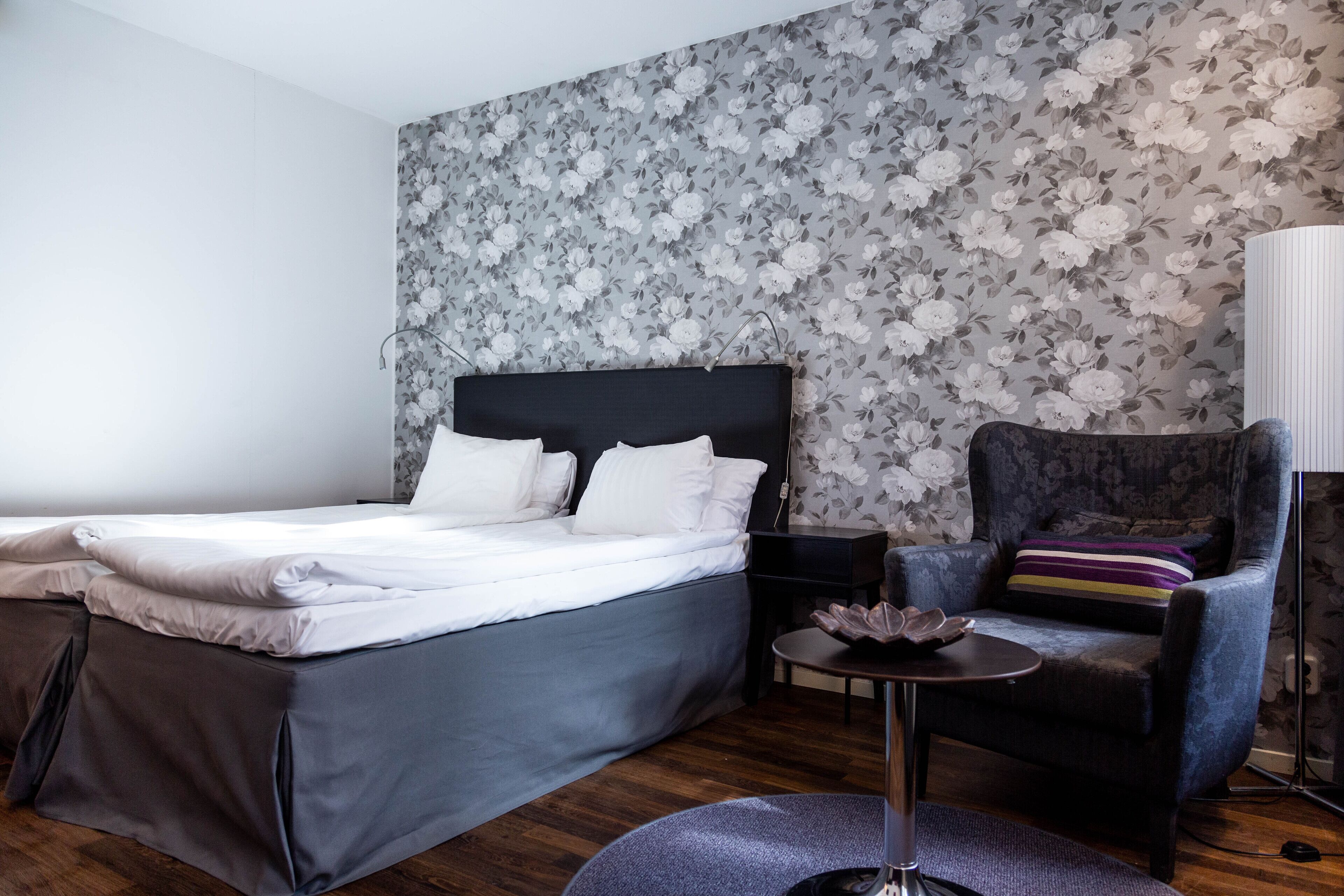A bedroom with a bed, a chair, a small table, and a lamp.