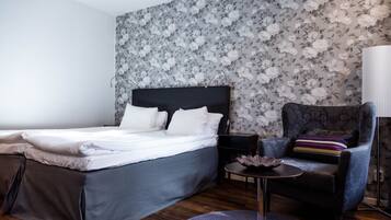 A bedroom with a bed, a chair, a small table, and a lamp.
