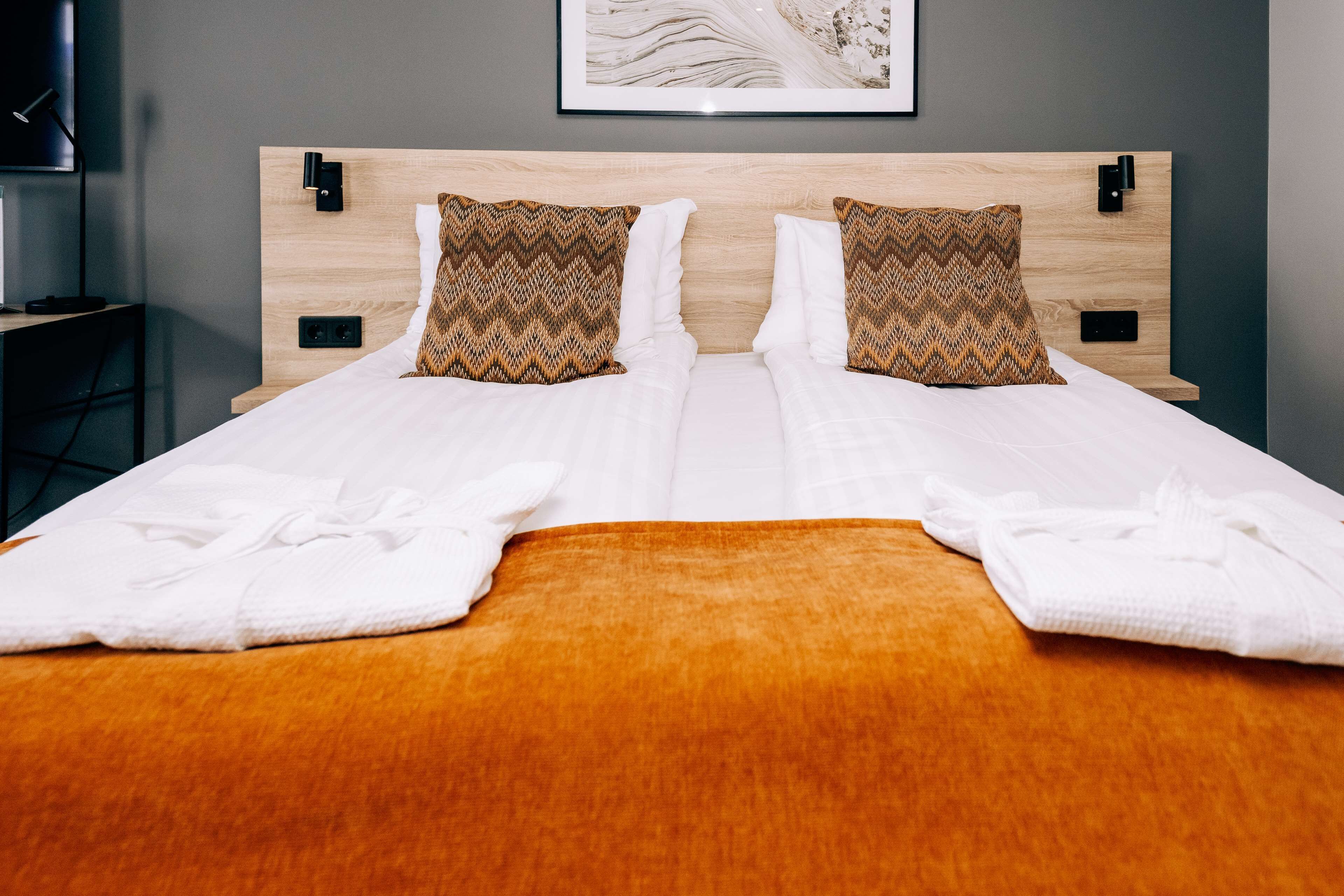 A neatly made double bed with two pillows, a wooden headboard, and a brown throw blanket.