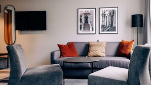 En moderne stue med en grå sofa, to lænestole, et rundt sofabord og et fladskærms-tv på væggen.