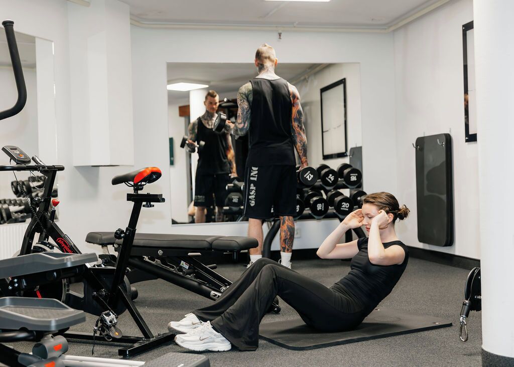 A gym with exercise equipment, a mirror, and a person performing sit-ups.