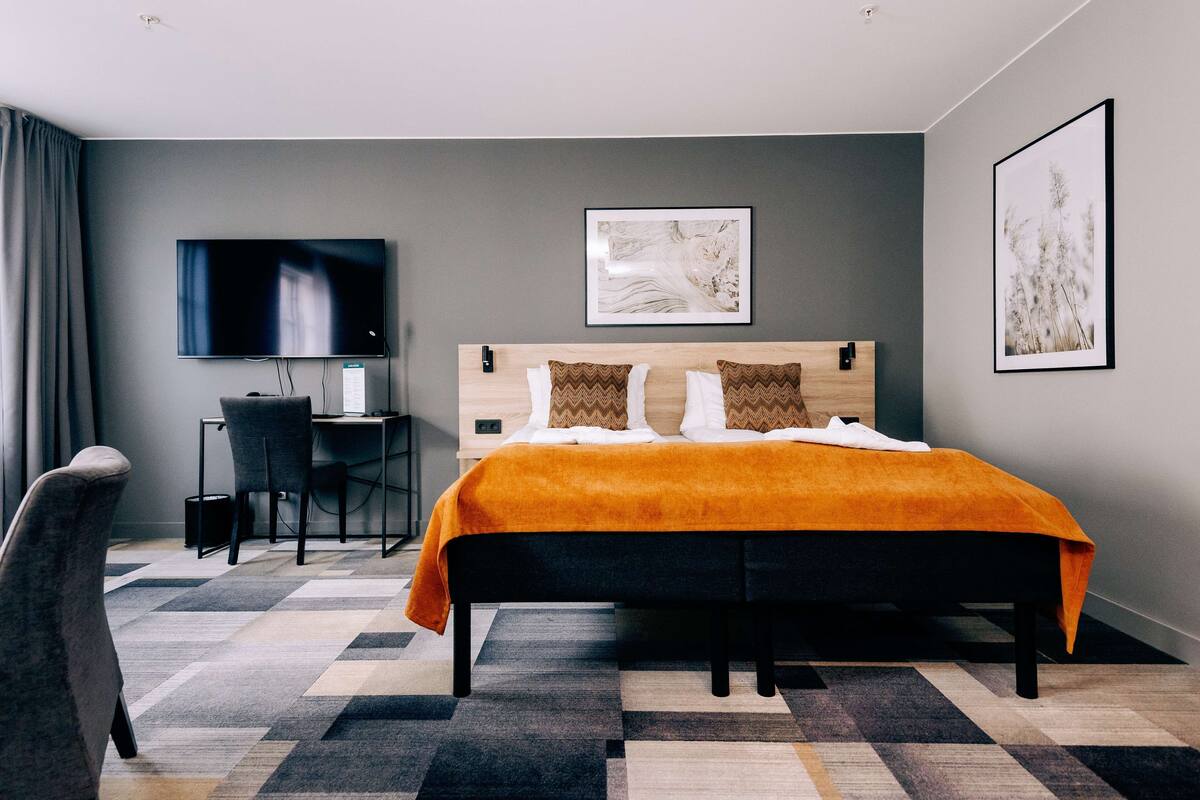 A modern hotel room with a large bed, a desk, and a television.