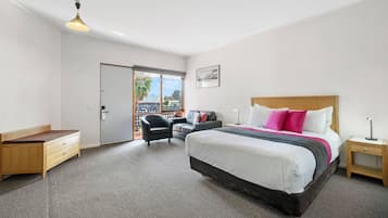 A hotel room with a bed, a desk, a chair, a nightstand, a lamp, and a view through a door.
