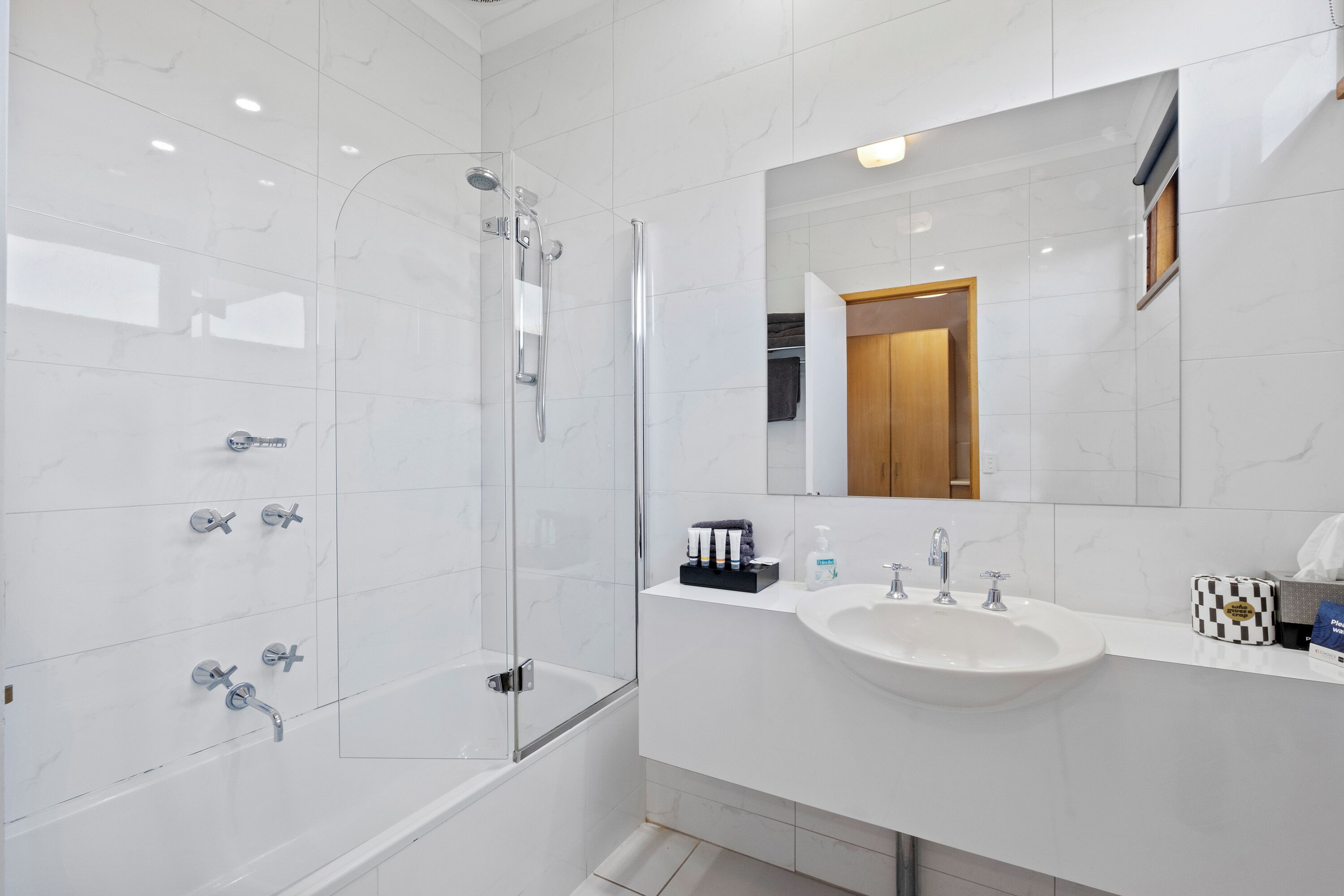 Un baño moderno con ducha envuelta en vidrio, un lavabo blanco y un espejo sobre el lavabo.