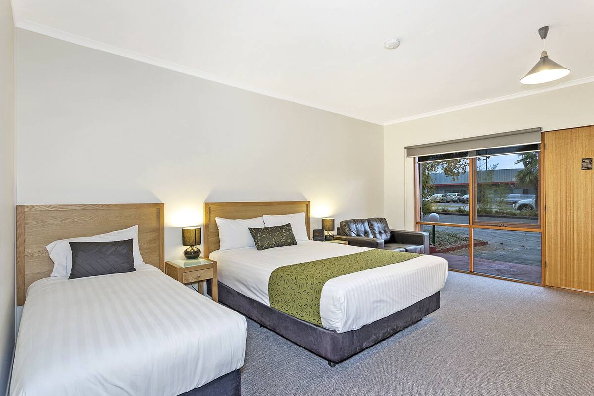 A hotel room with two beds, a large window, a desk, and a chair.