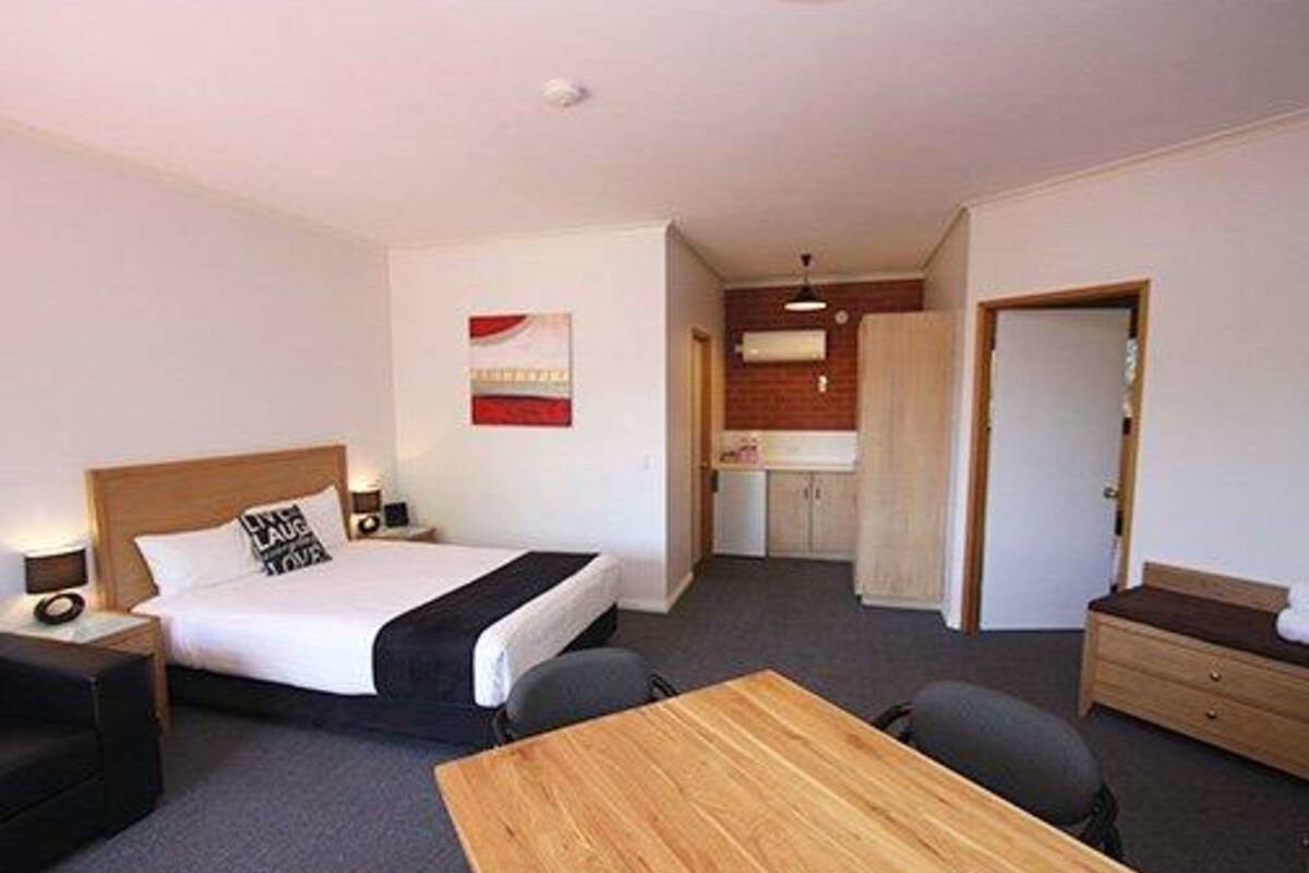 A hotel room with a bed, bedside table, lamp, and a small desk with a chair.