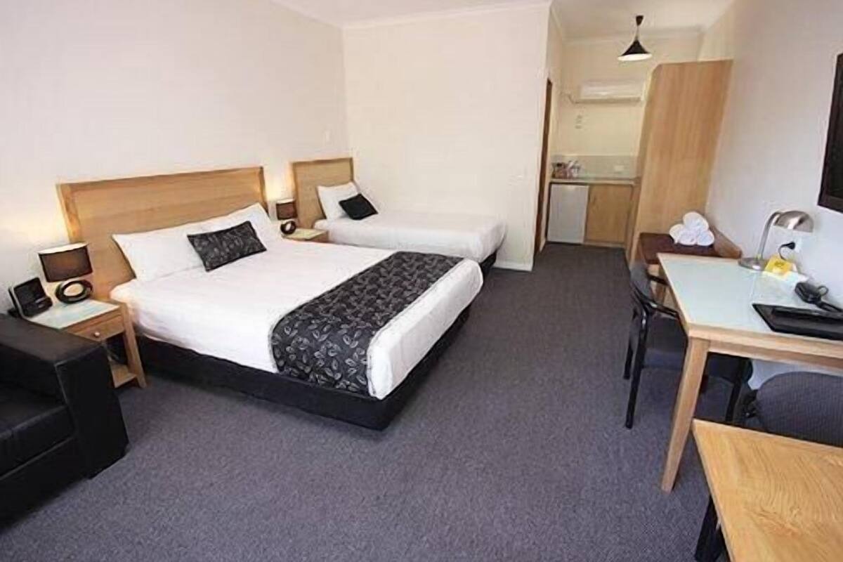 A hotel room with a bed, bedside tables, a desk, a chair, and a small kitchenette.
