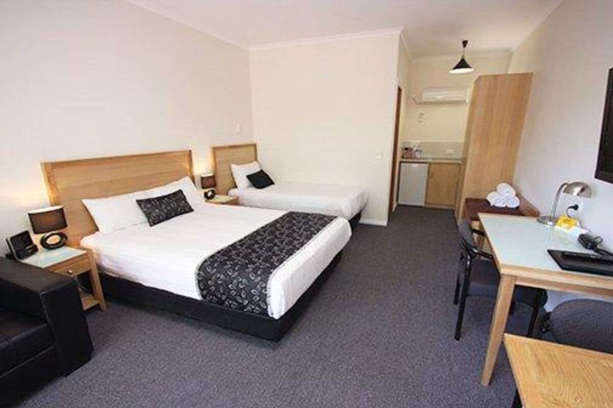 Ein Hotelzimmer mit Doppelbett, Schreibtisch, Stuhl, einer kleinen Küchenzeile und einem Badezimmer.