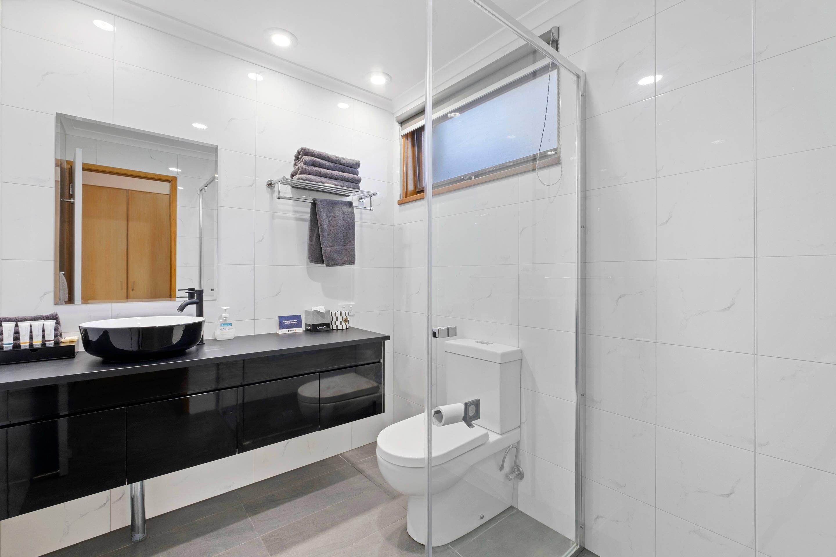 A modern bathroom with a black vanity, white tiles, a glass shower enclosure, and a toilet.