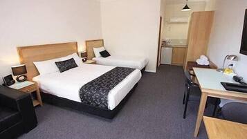 A hotel room with a bed, bedside tables, a desk, a chair, and a small kitchenette.
