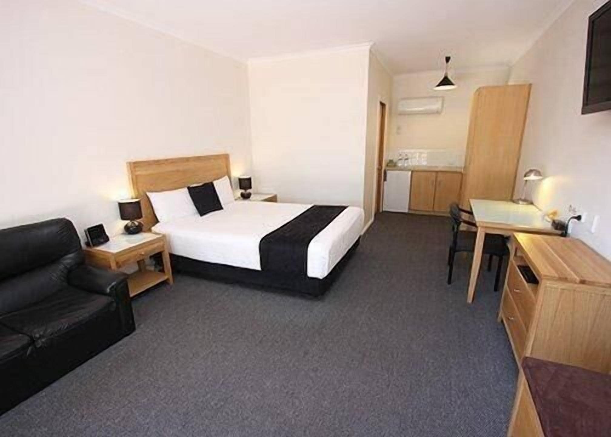 Een hotelkamer met een bed, een bureau, een stoel, een klein keukenhoekje en een televisie.