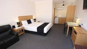 Een hotelkamer met een bed, een bureau, een stoel, een klein keukenhoekje en een televisie.
