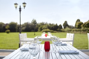Een eettafel buiten opgesteld, met stoelen, een rode vaas en glazen.