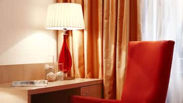 Una habitación de hotel con un escritorio de madera, una silla roja, una lámpara y cortinas.