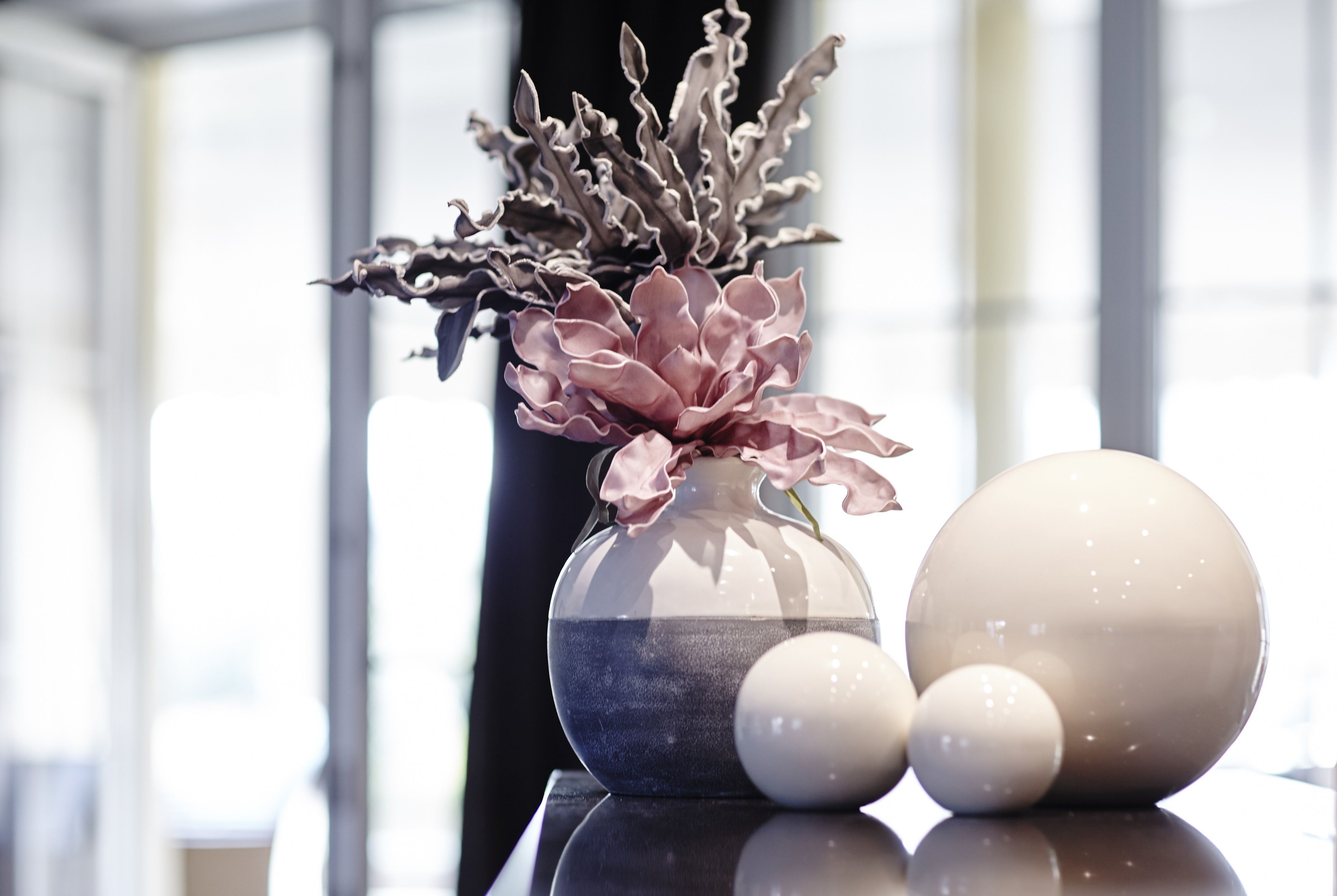 Un vase contenant des fleurs roses et des objets sphériques, le tout posé sur une surface réfléchissante.