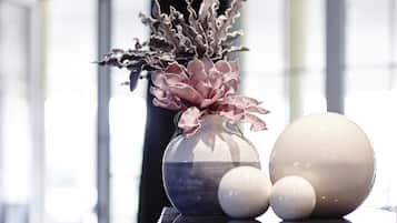 Un vase contenant des fleurs roses et des objets sphériques, le tout posé sur une surface réfléchissante.