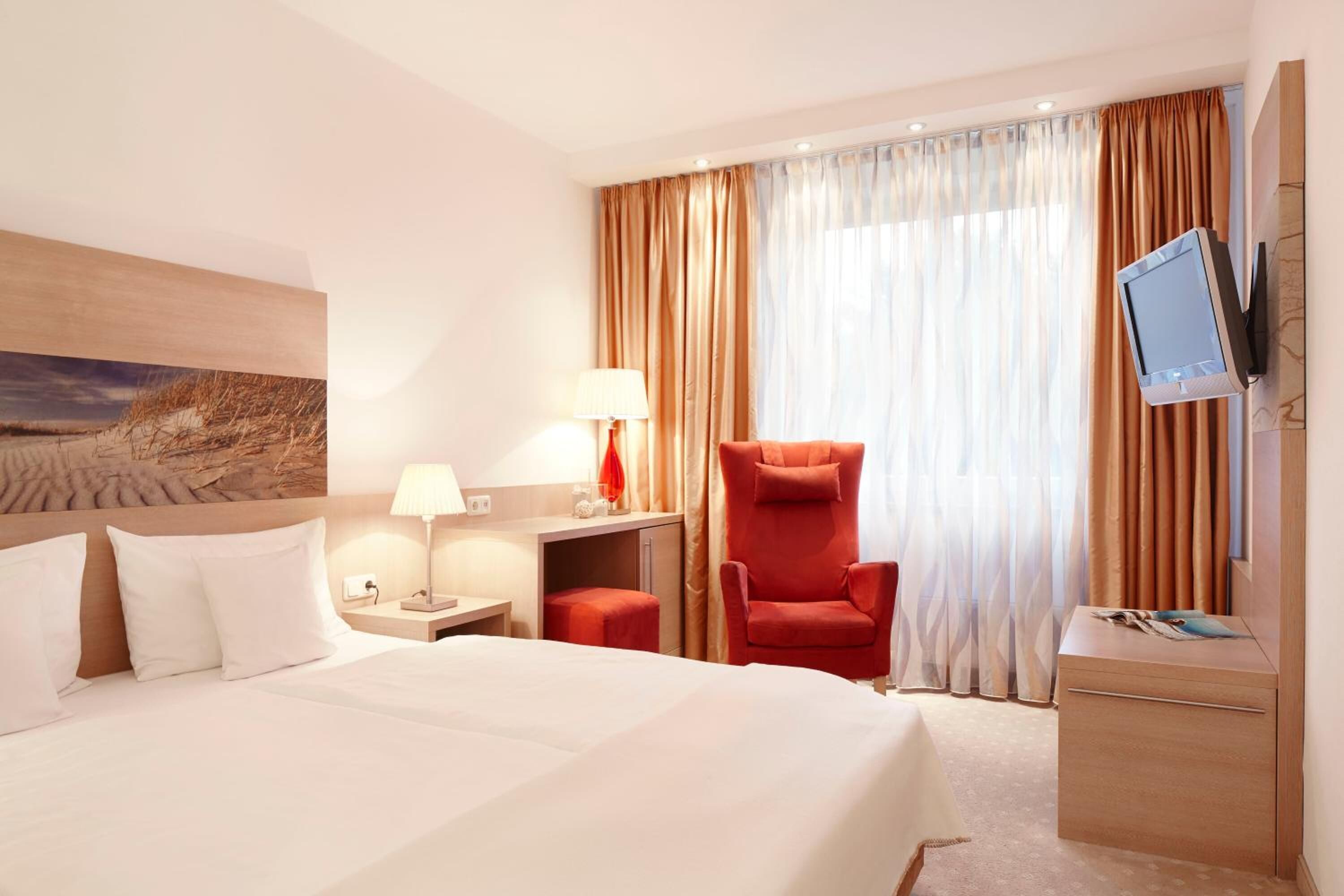 A hotel room with a bed, a desk, a chair, a TV, and a window with curtains.