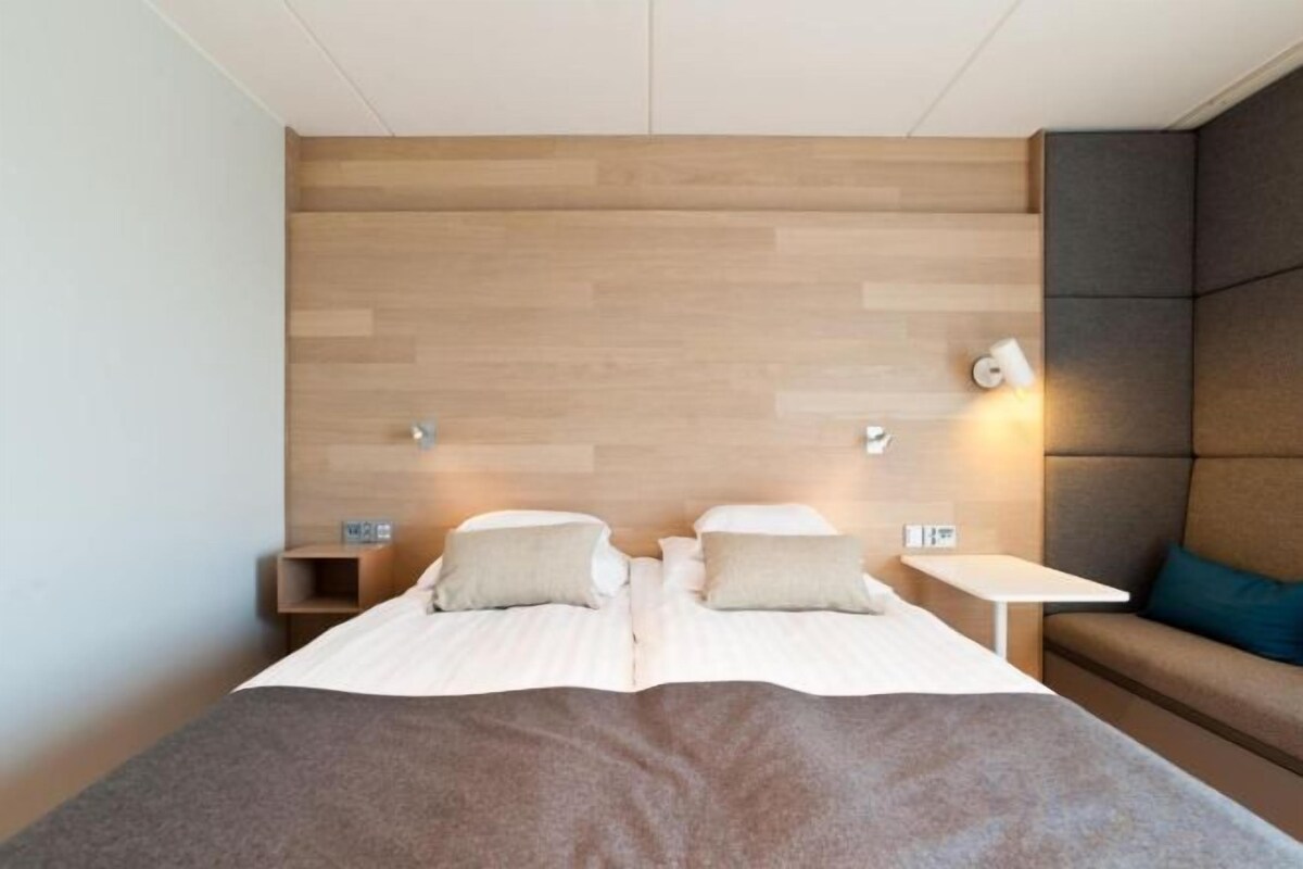 A hotel room with a bed, bedside tables, a nightstand, and a seating area with a cushion.