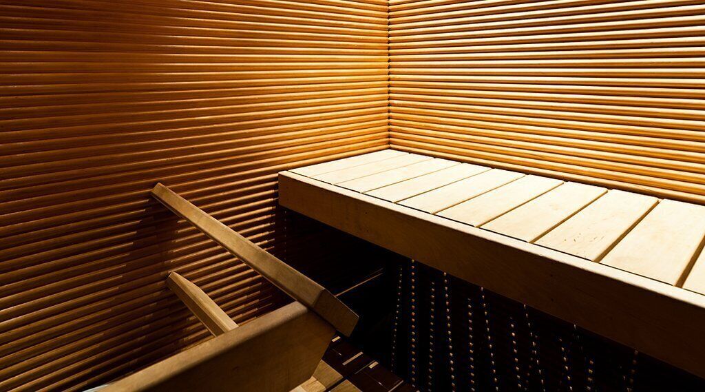 A corner of a room with wooden slatted walls and a bench.
